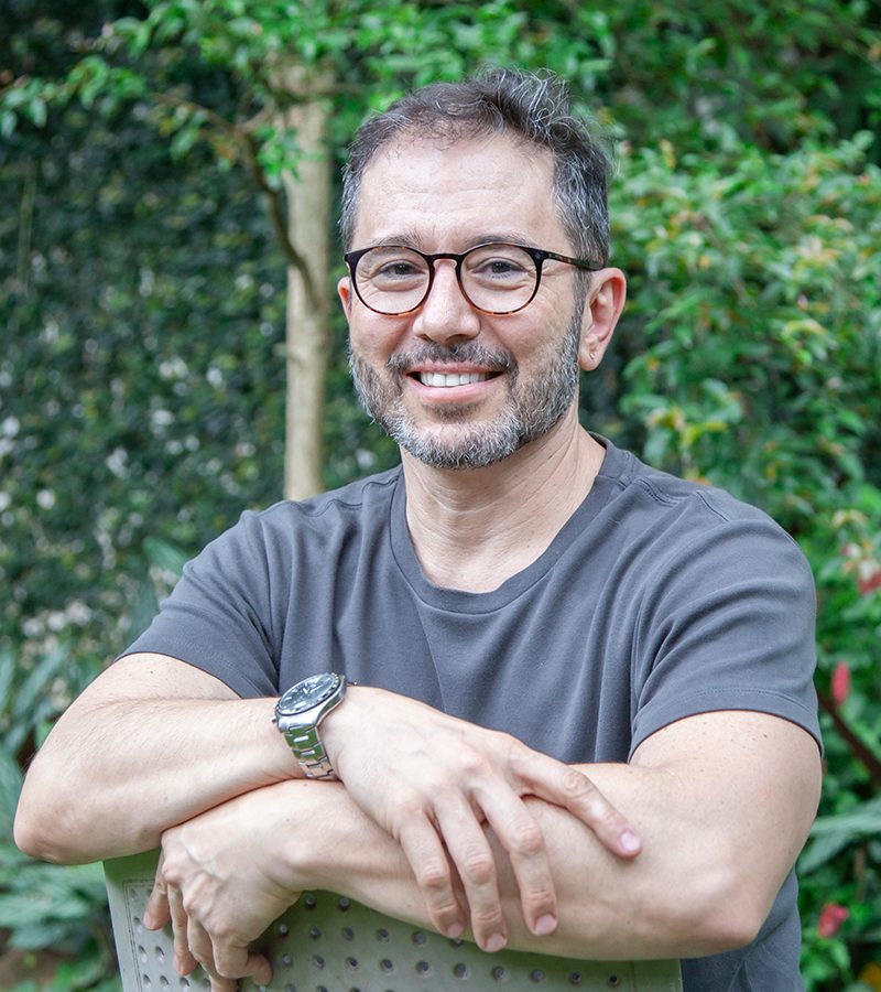 Alessandro Estrella, consultor, sorrindo, com barba grisalha e braços semi-cruzados.